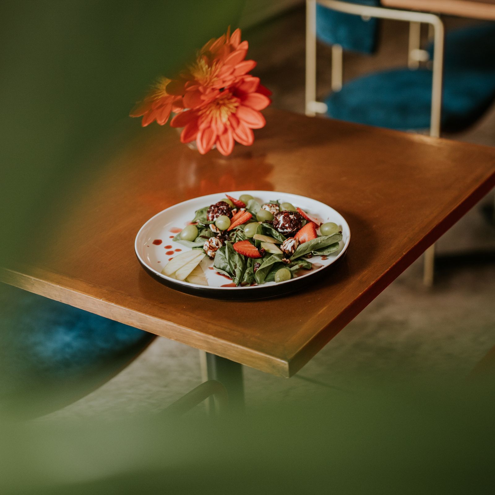 A colorful salad with fresh vegetables on a wooden table, complemented by vibrant flowers.